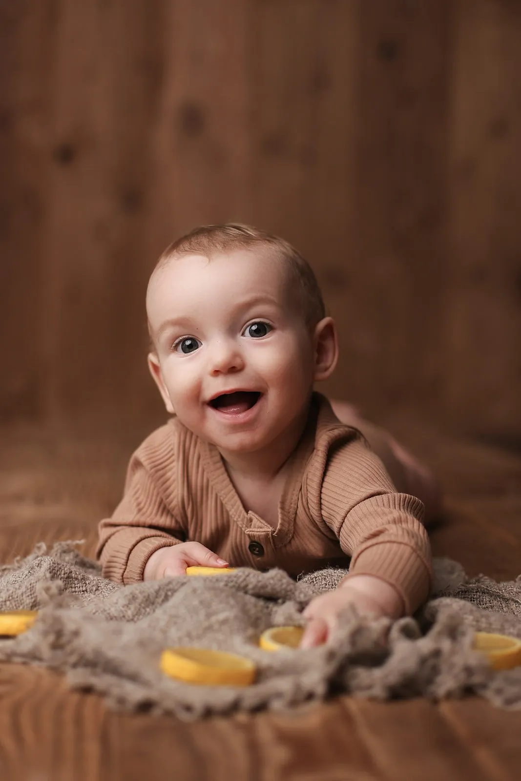 Bébé souriant sur le ventre en tenue camel, séance bébé en studio près de Toulouse