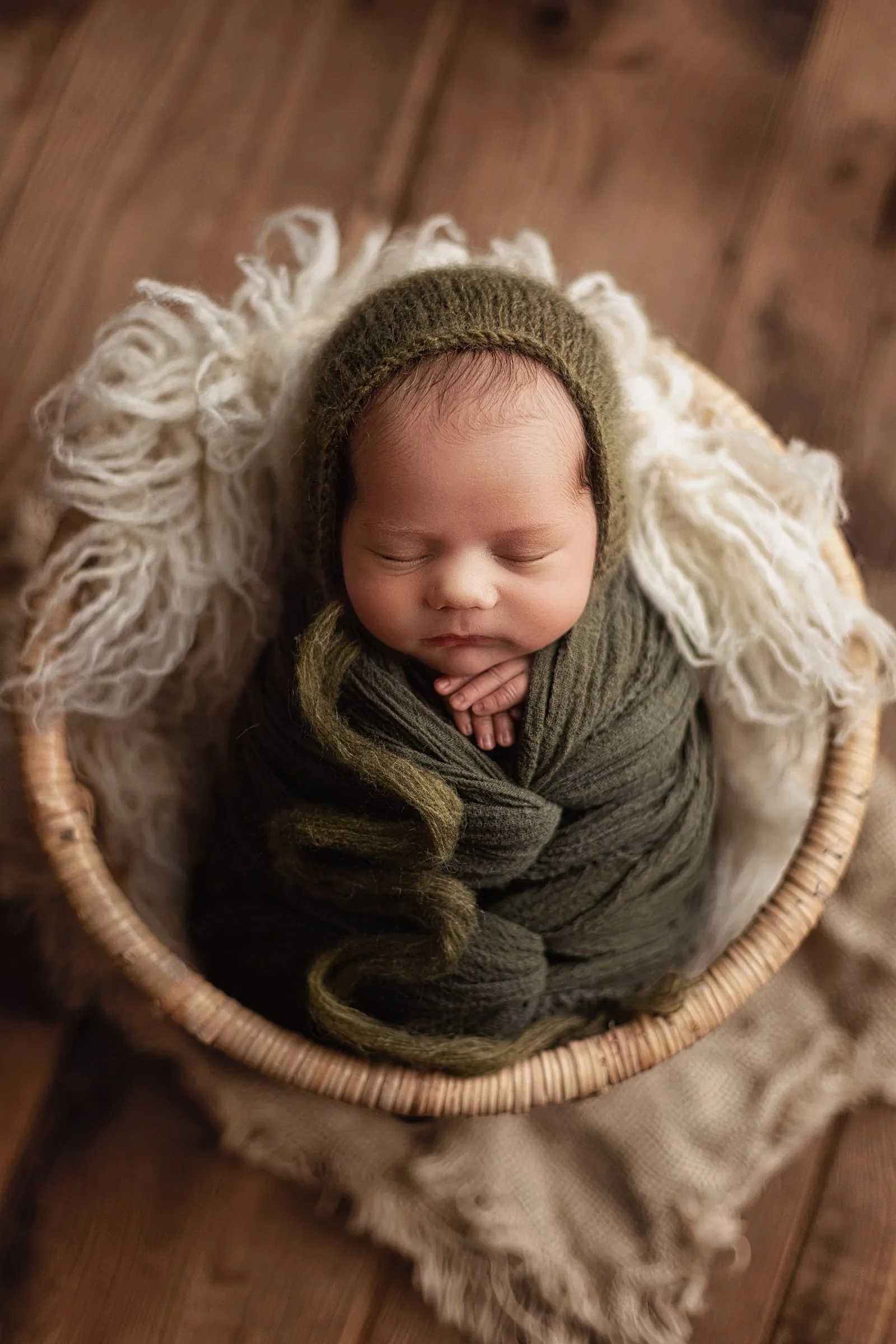 Nouveau-né emmailloté de vert dans un panier en osier, séance photo en studio