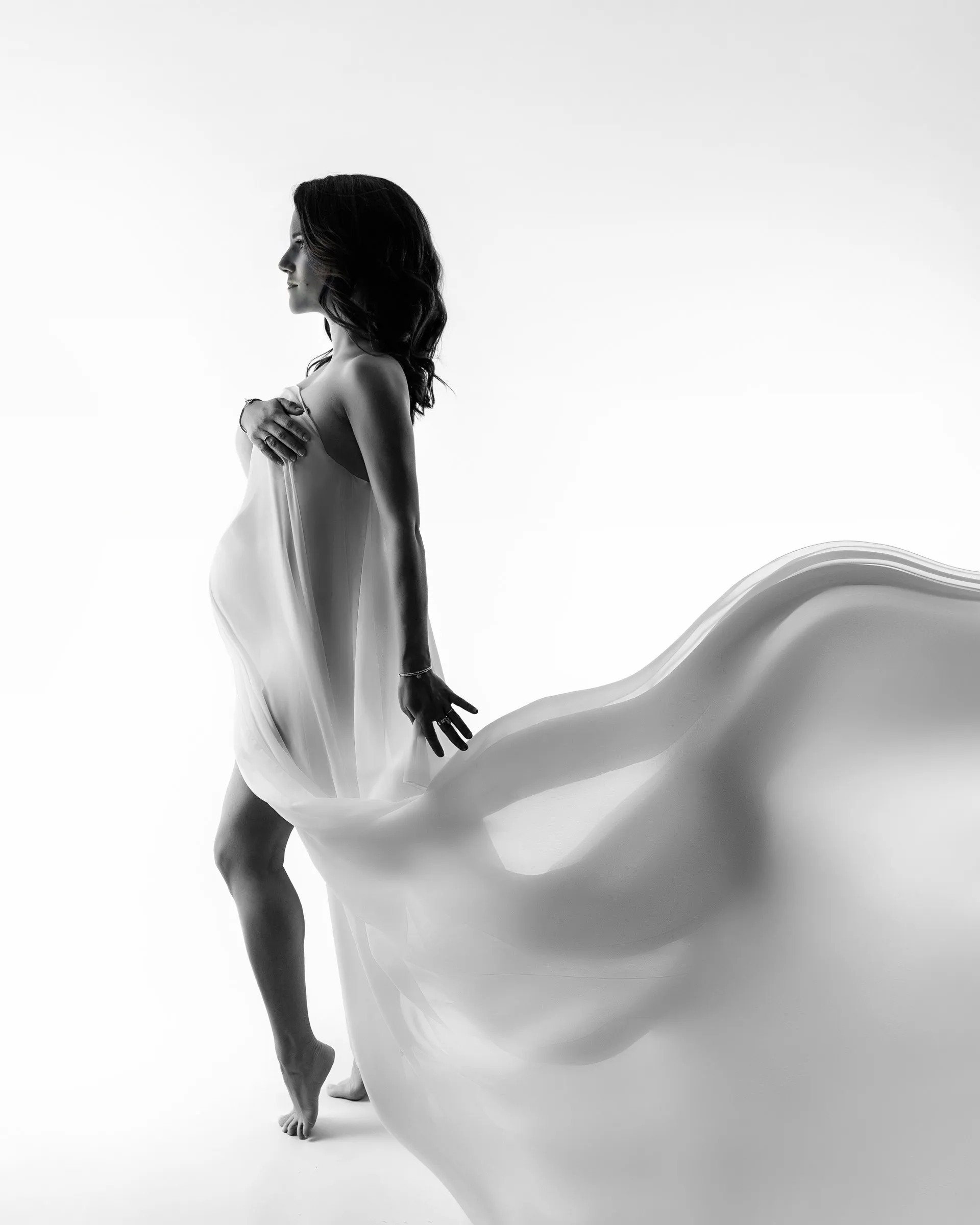 Portrait de grossesse artistique sur fond clair, voile en mouvement