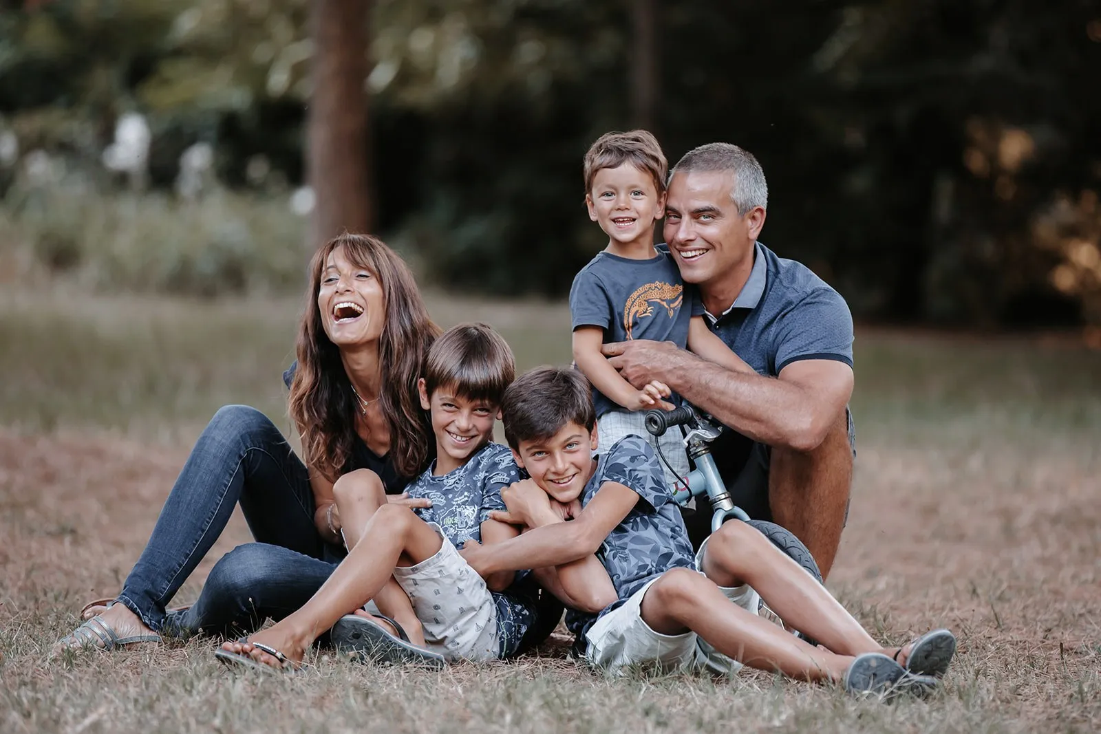 Famille de six qui rit dans l'herbe, séance photo famille en extérieur près de Toulouse