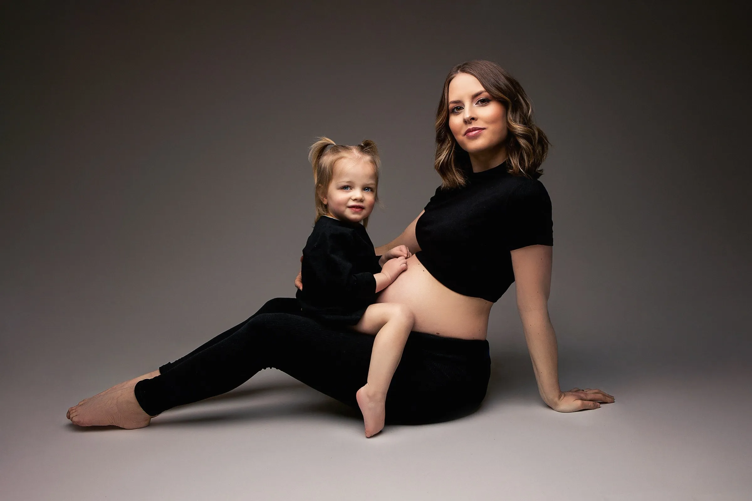 Maman enceinte et sa petite fille assises en studio, séance grossesse en famille