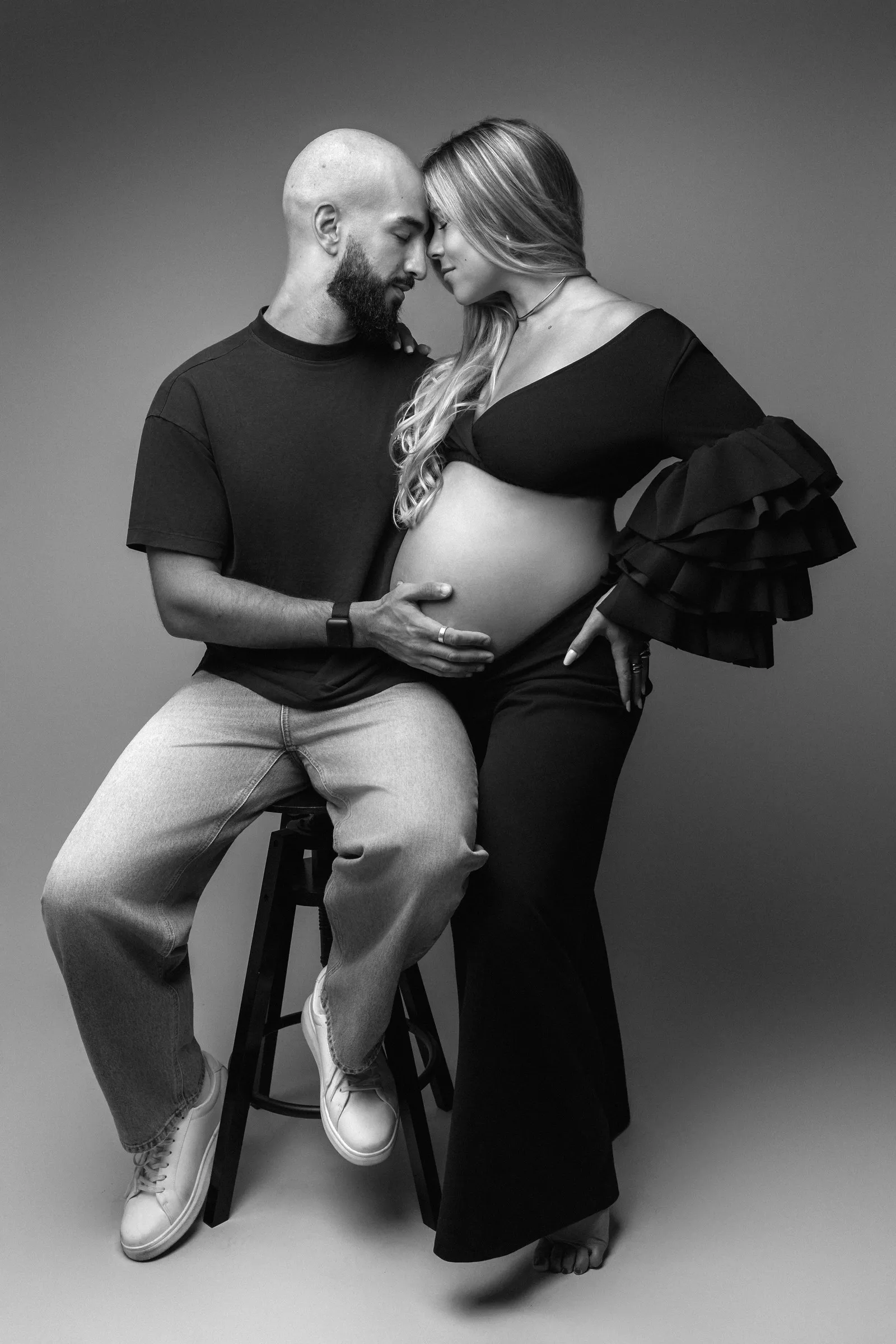 Futurs parents front contre front, la main du papa sur le ventre, séance photo grossesse en couple en noir et blanc au studio près de Toulouse