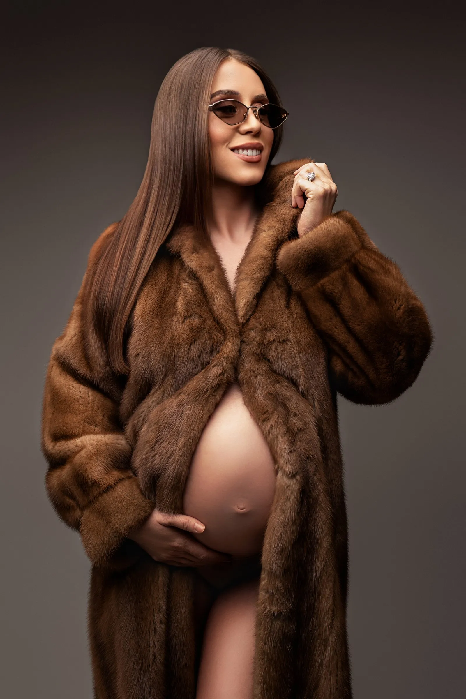 Future maman en manteau de fourrure ouvert, séance grossesse en studio