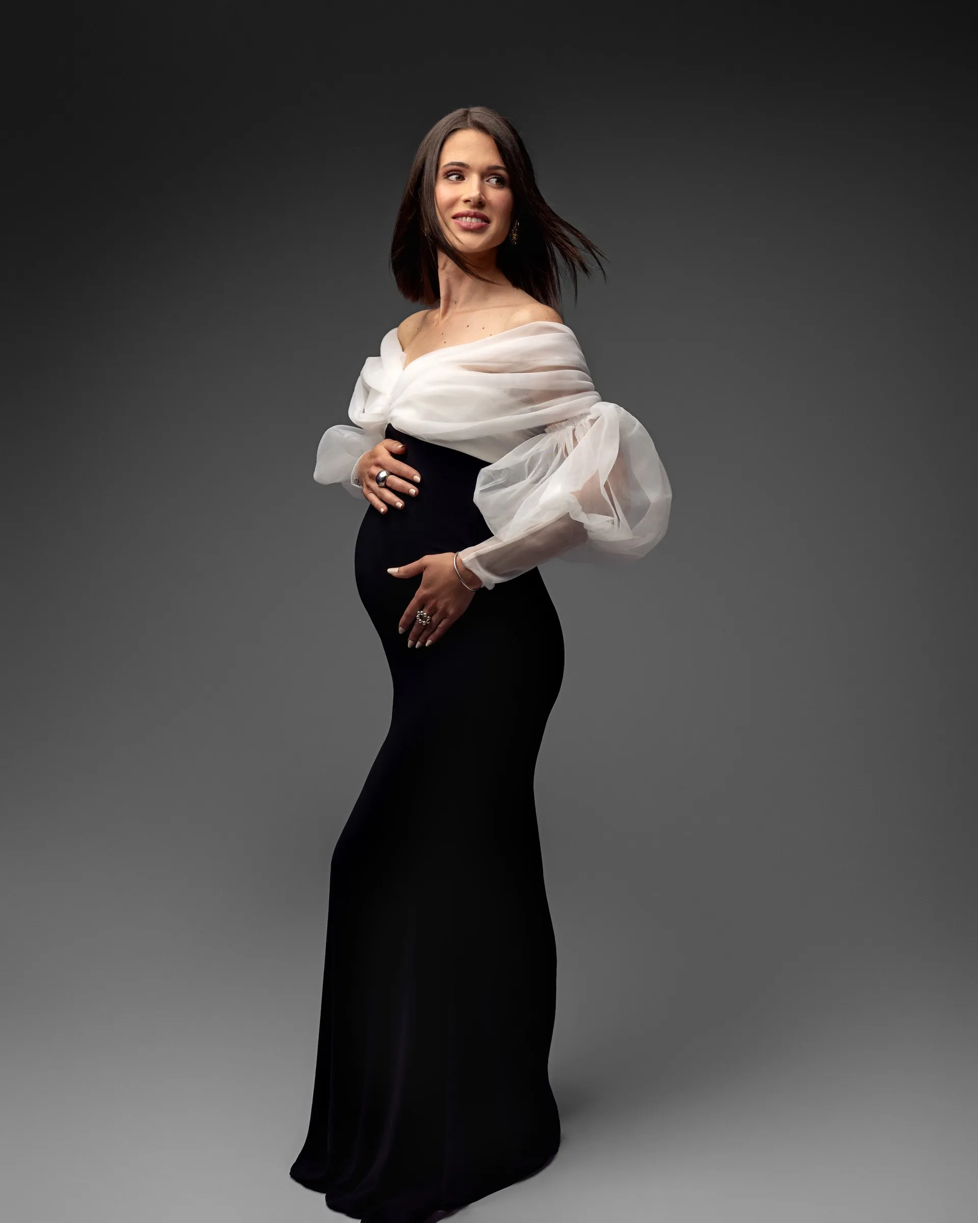 Future maman en robe noire à manches blanches, séance grossesse en studio