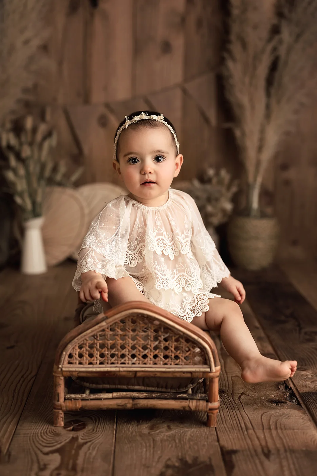 Bébé assis dans un fauteuil en rotin, robe en dentelle, séance bébé par Emilie Colusso photographe