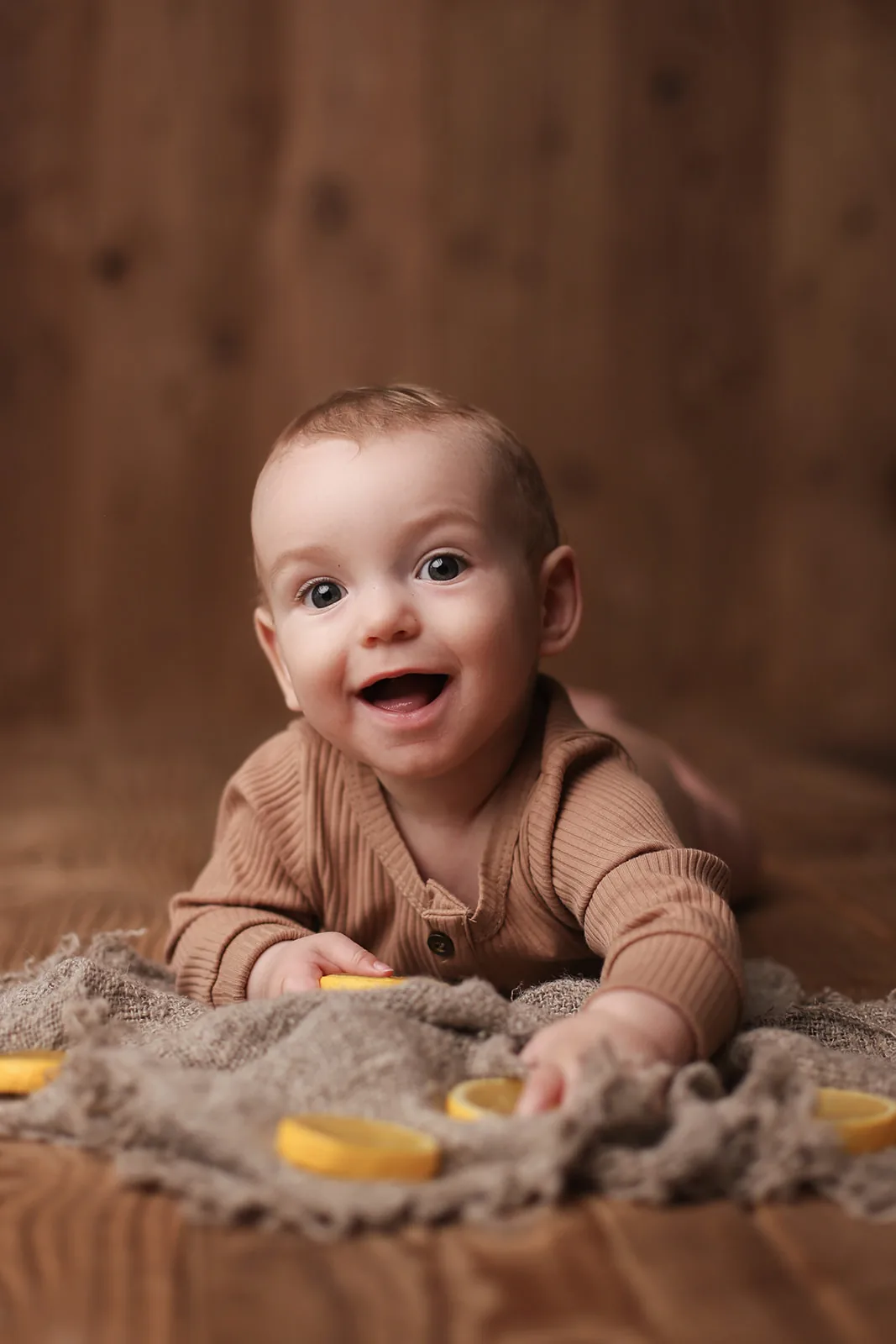 Bébé souriant sur le ventre en tenue camel, séance photo bébé en studio