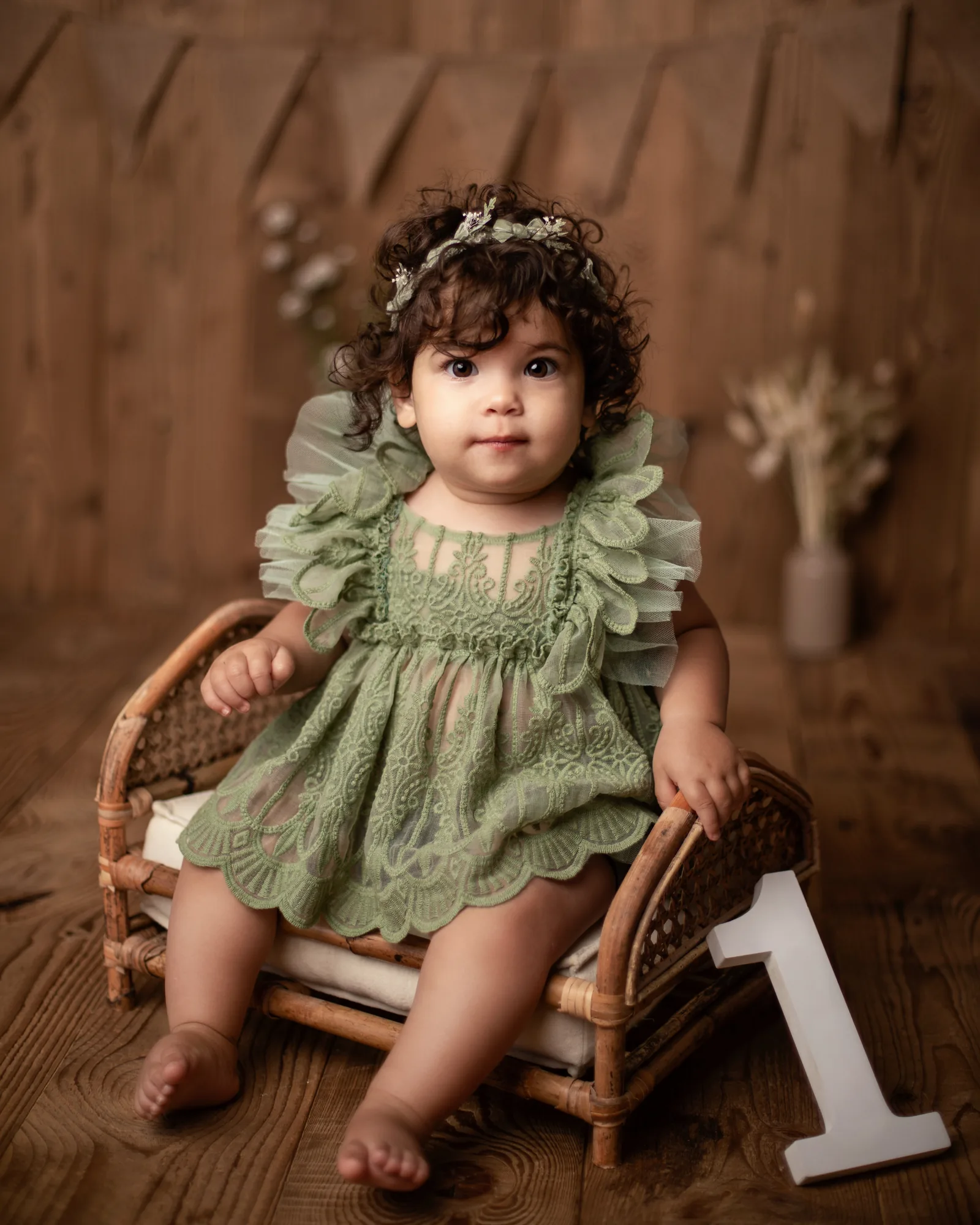 Bébé d'un an en robe verte sur un fauteuil en rotin, séance photo au studio, Emilie Colusso photographe