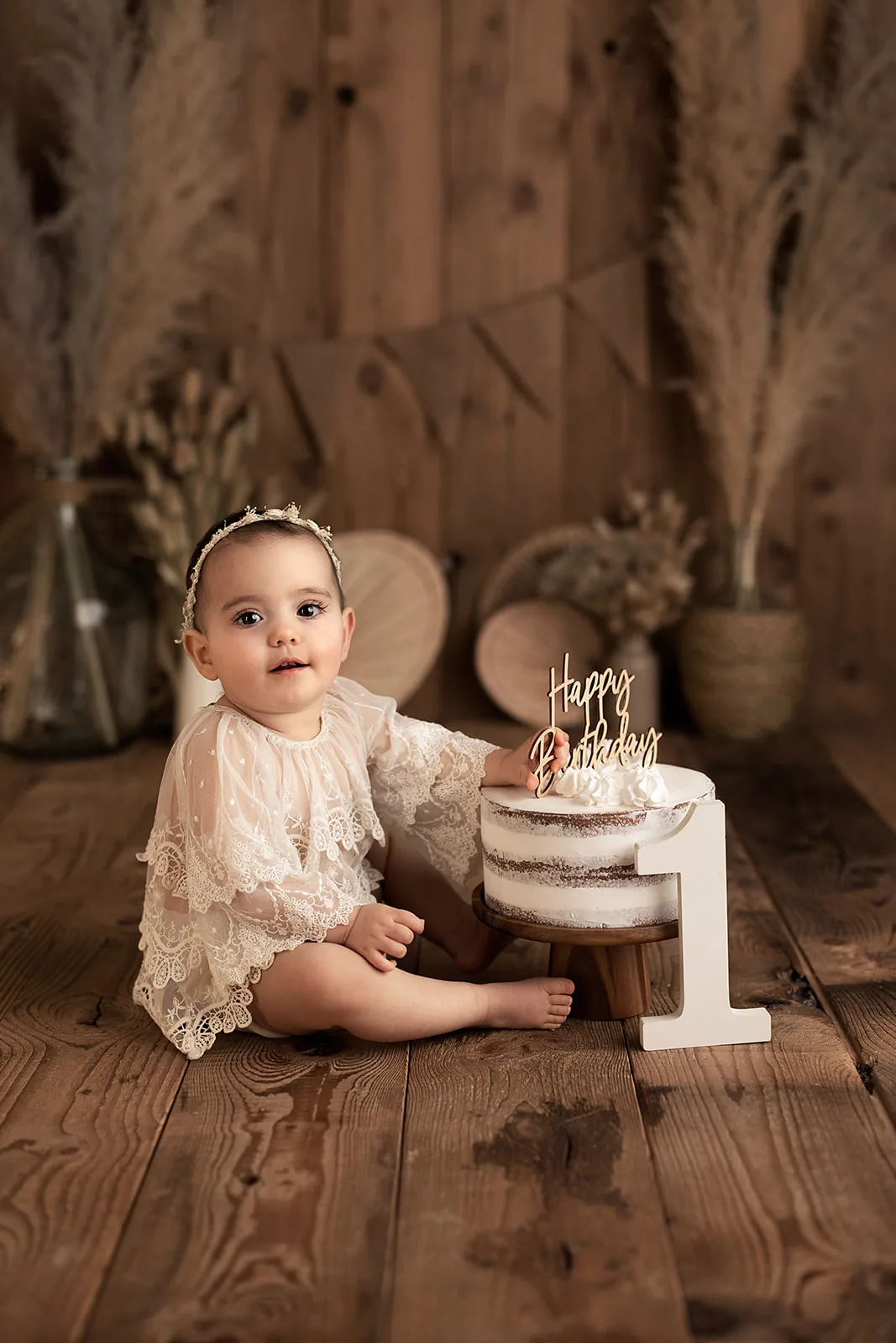 Séance Smash Cake en studio près de Toulouse, bébé en robe de dentelle devant son gâteau dans un décor bohème, Emilie Colusso photographe