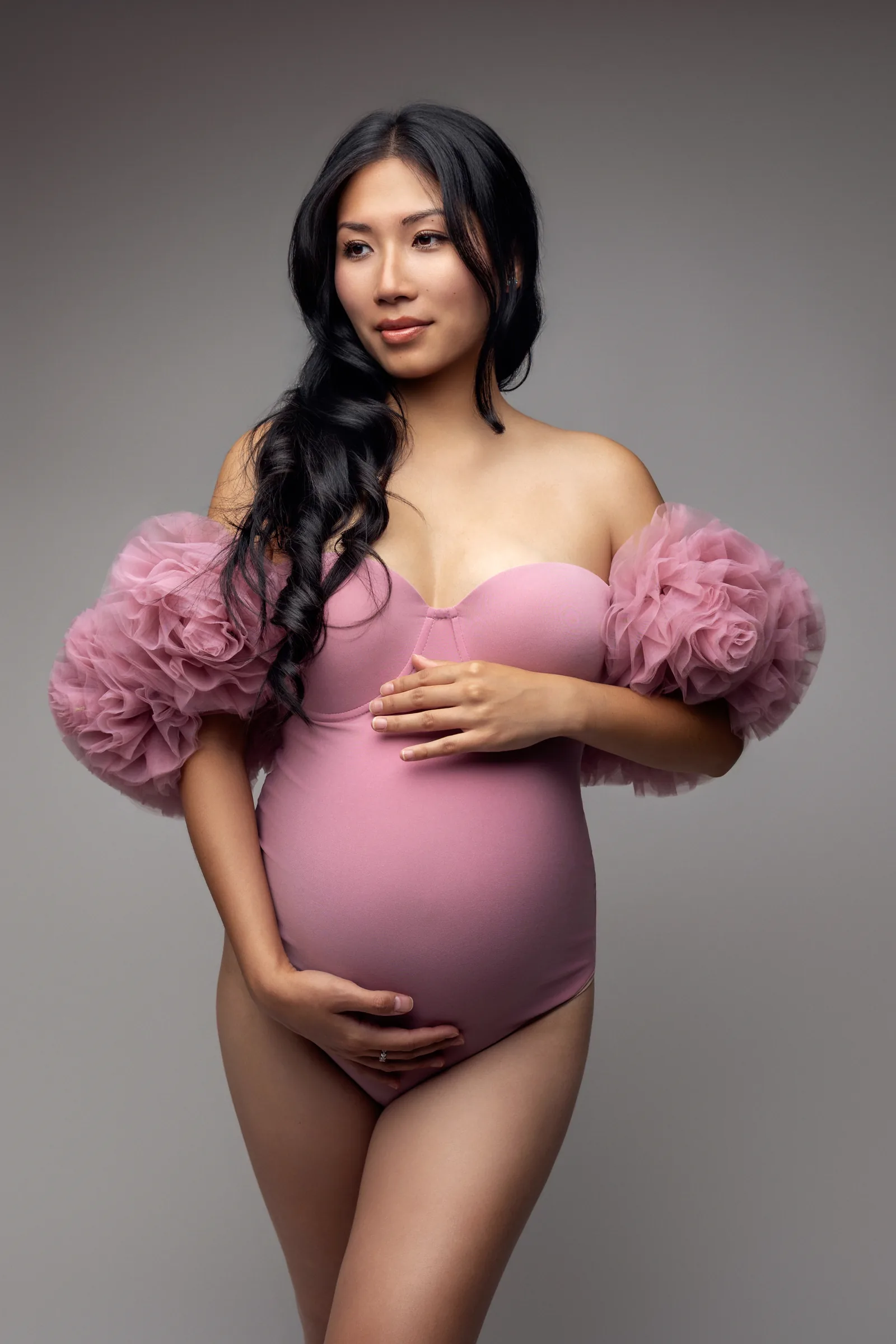 Future maman en body rose à manches de tulle, photo de grossesse en studio par Emilie Colusso