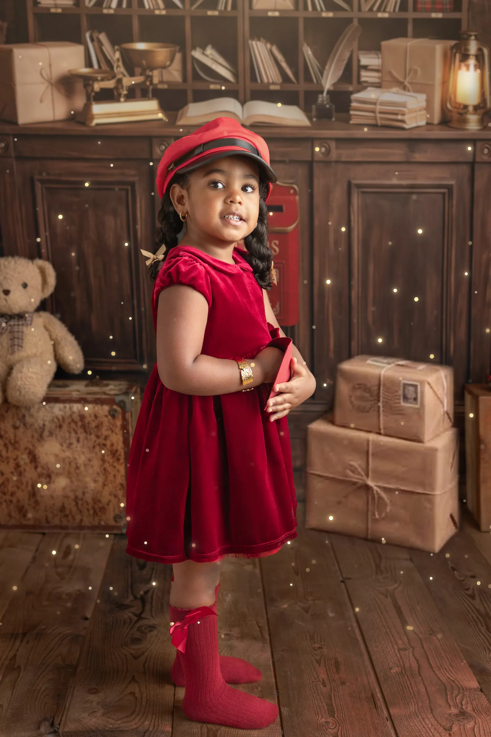 Petite fille en robe de velours rouge devant la boîte aux lettres rouge du décor bureau de poste du Père Noël, studio Emilie Colusso à Roquettes près de Toulouse